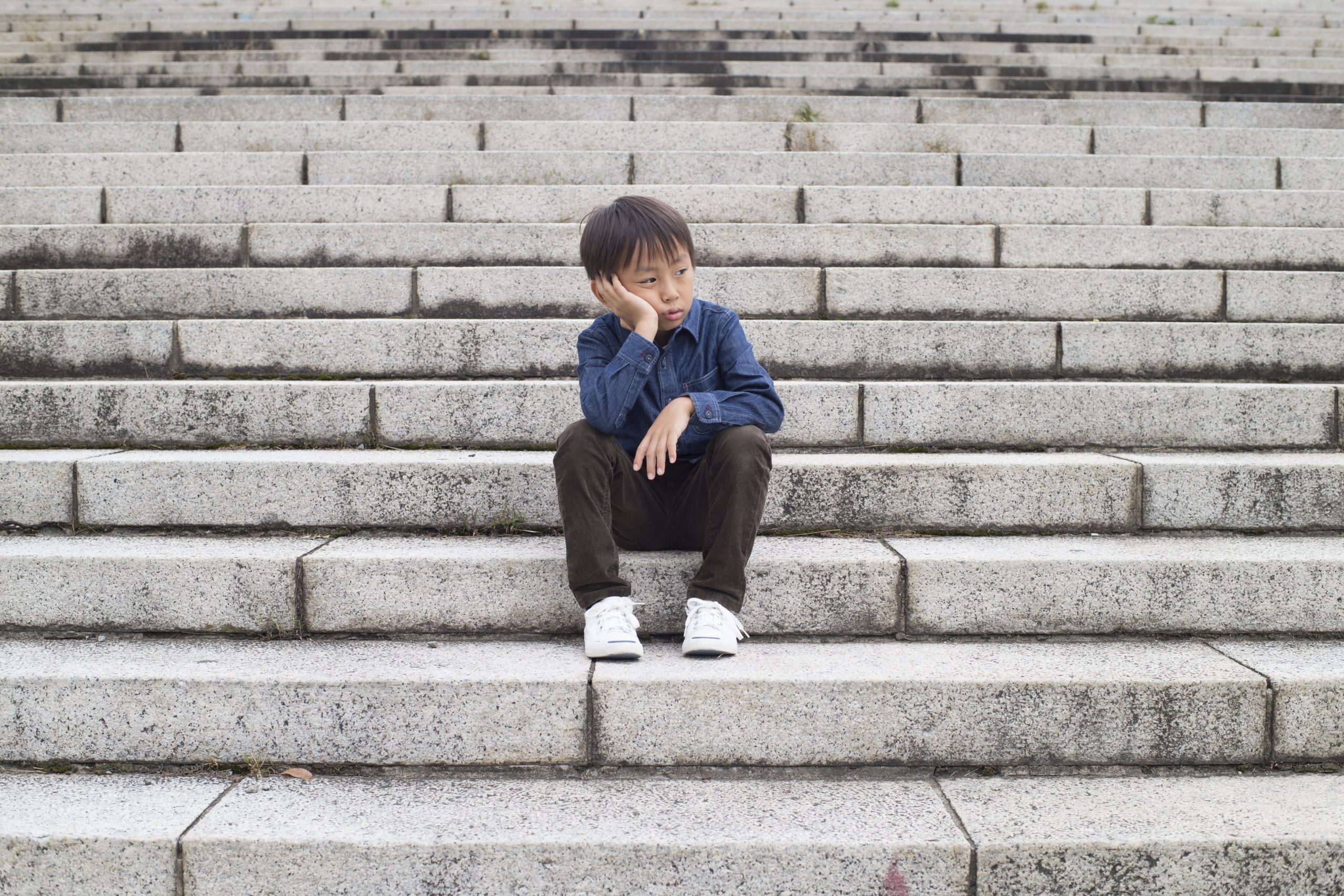 Depressed boy sitting alone on stone steps
