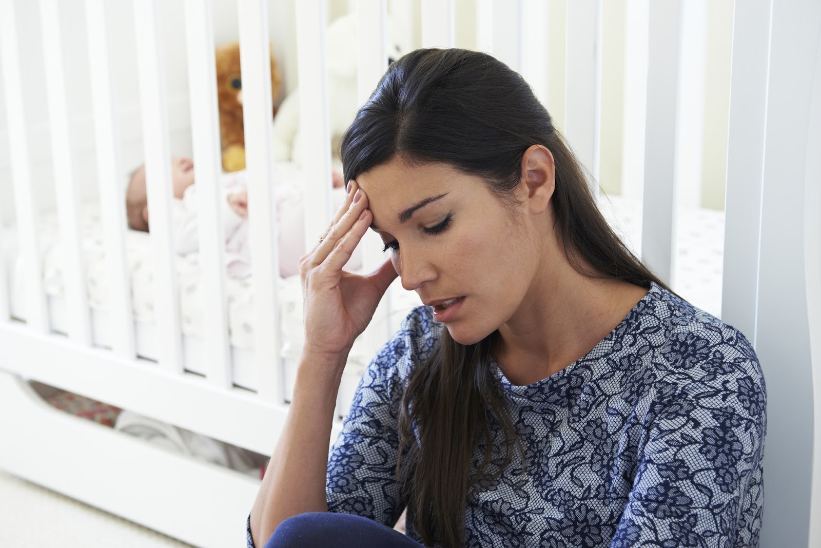 Overwhelmed and distressed mom sitting in front of a crib