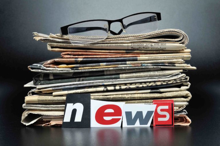 glasses on top of newspaper stack with news words in front Courtesy of